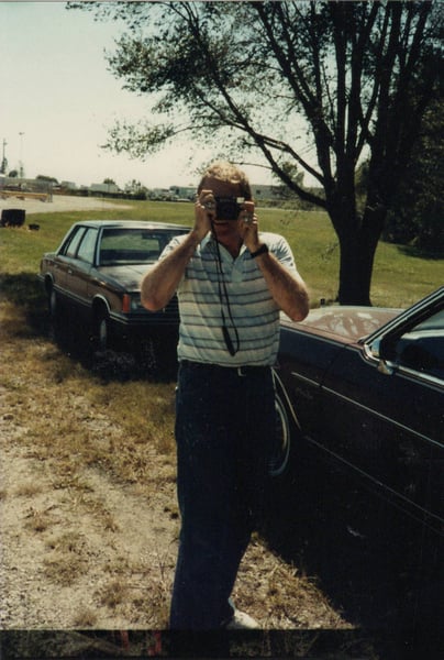 Man holding camera in front of oldsmobile car